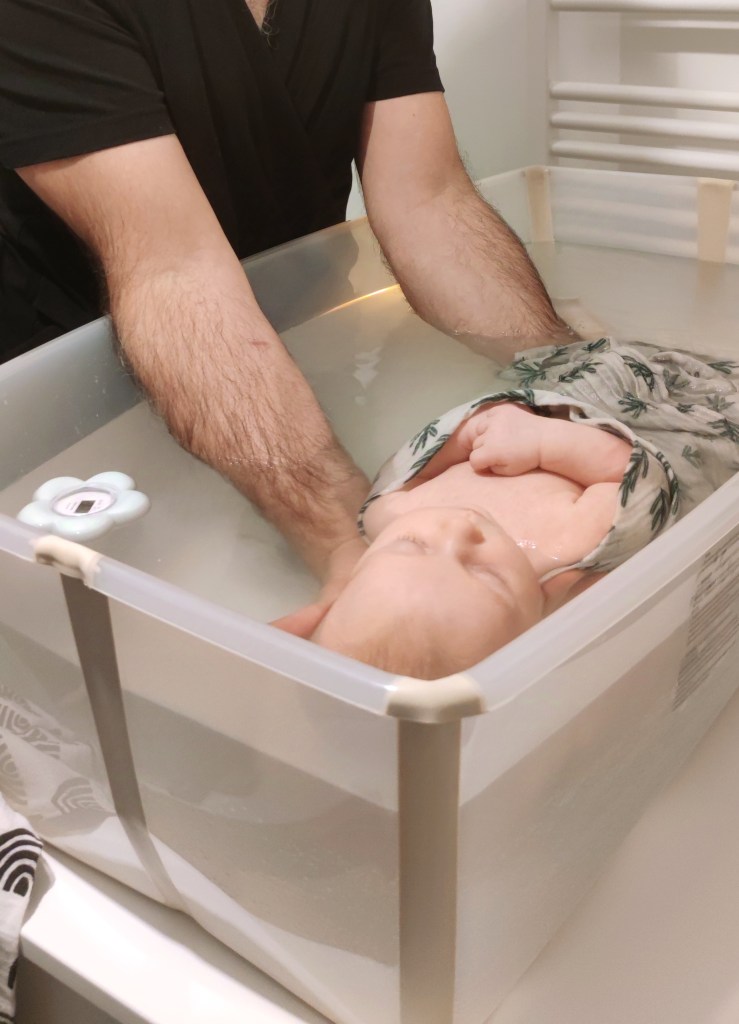 Bébé emmalloté dans une baignoire et tenue par son père